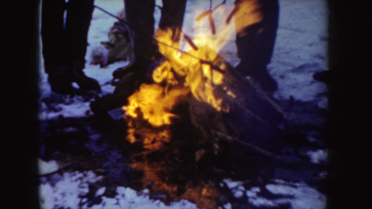 1955 Idaho 8mm frame showing bundled people from the knees down near orange flames on snow.