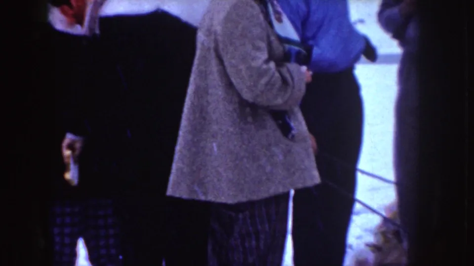 A 1955 Idaho home-movie frame shows bundled adults near snow, one holding a camera at chest height.