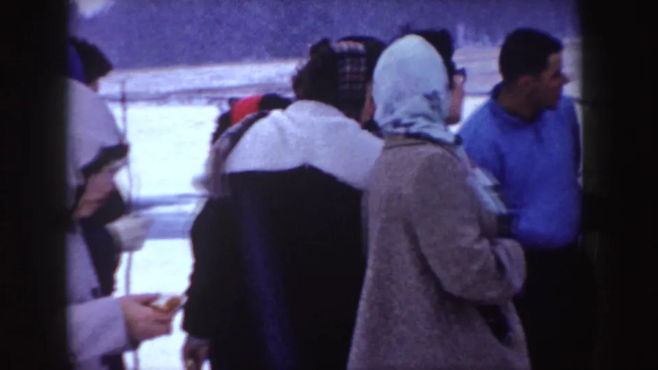 Bundled adults in 1955 Idaho stand together in a snowy outdoor area after warming by the fire.