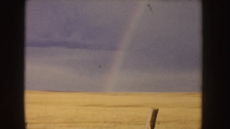 A wide Idaho field appears under a cloudy sky, with a faint rainbow visible near the right side of the frame.