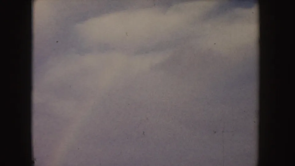 1955 Idaho 8mm view of open tan farmland and puffy white clouds, with a dark vertical border splitting the frame.