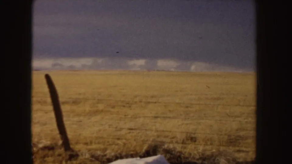 A 1955 8mm frame shows an open Idaho field or roadside view under a dark sky, partially blocked by vertical film or window edges.