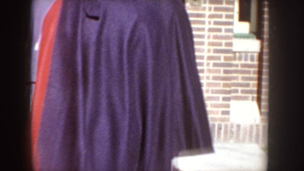 1955 Idaho home-movie frame showing dark overcoats in the foreground beside brickwork and a doorway.