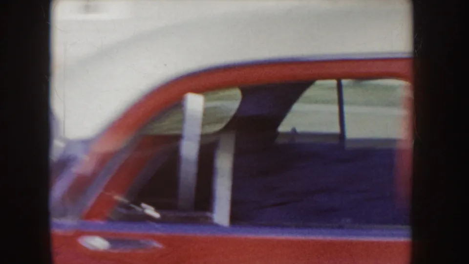 The red sedan passes very close to the camera, leaving a cropped view of its side window, roofline, and door frame.