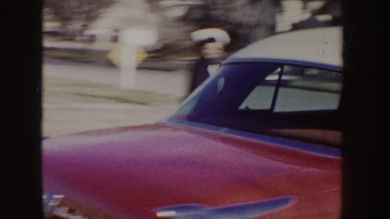 Red-and-white classic car beside a uniformed woman near a suburban street.