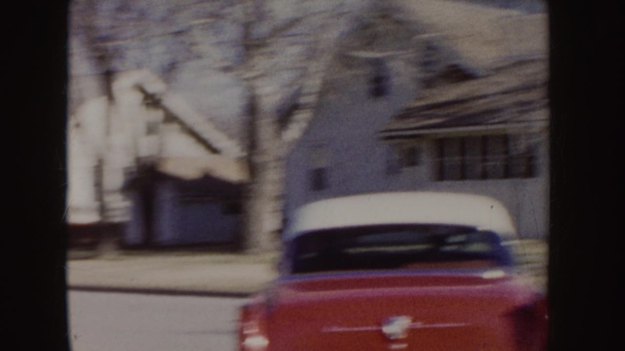 Rear view of a red-and-white car on a residential street with houses behind it.