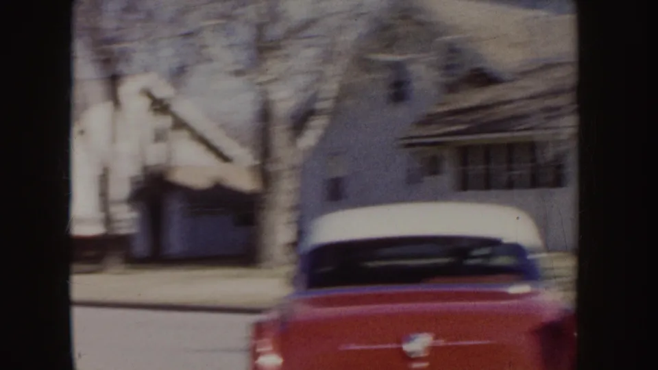 1955 Idaho frame with the rear of a red-and-white classic car on a quiet residential street lined with houses and bare trees.