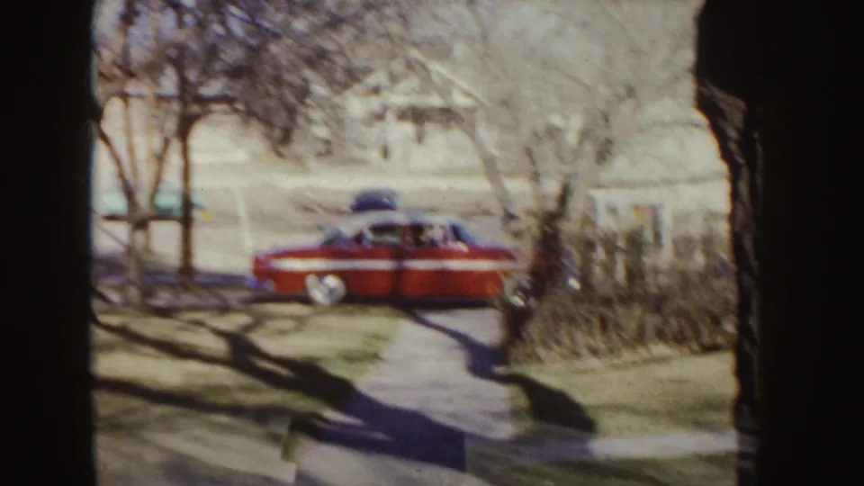 A red mid-century car sits near a sidewalk in a quiet Idaho neighborhood with bare trees and houses visible.