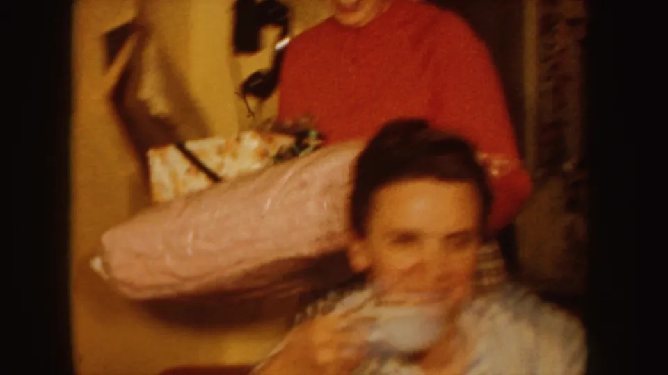 The indoor 1955 Idaho scene shows a woman drinking from a teacup, with another person partly visible in the warm background.