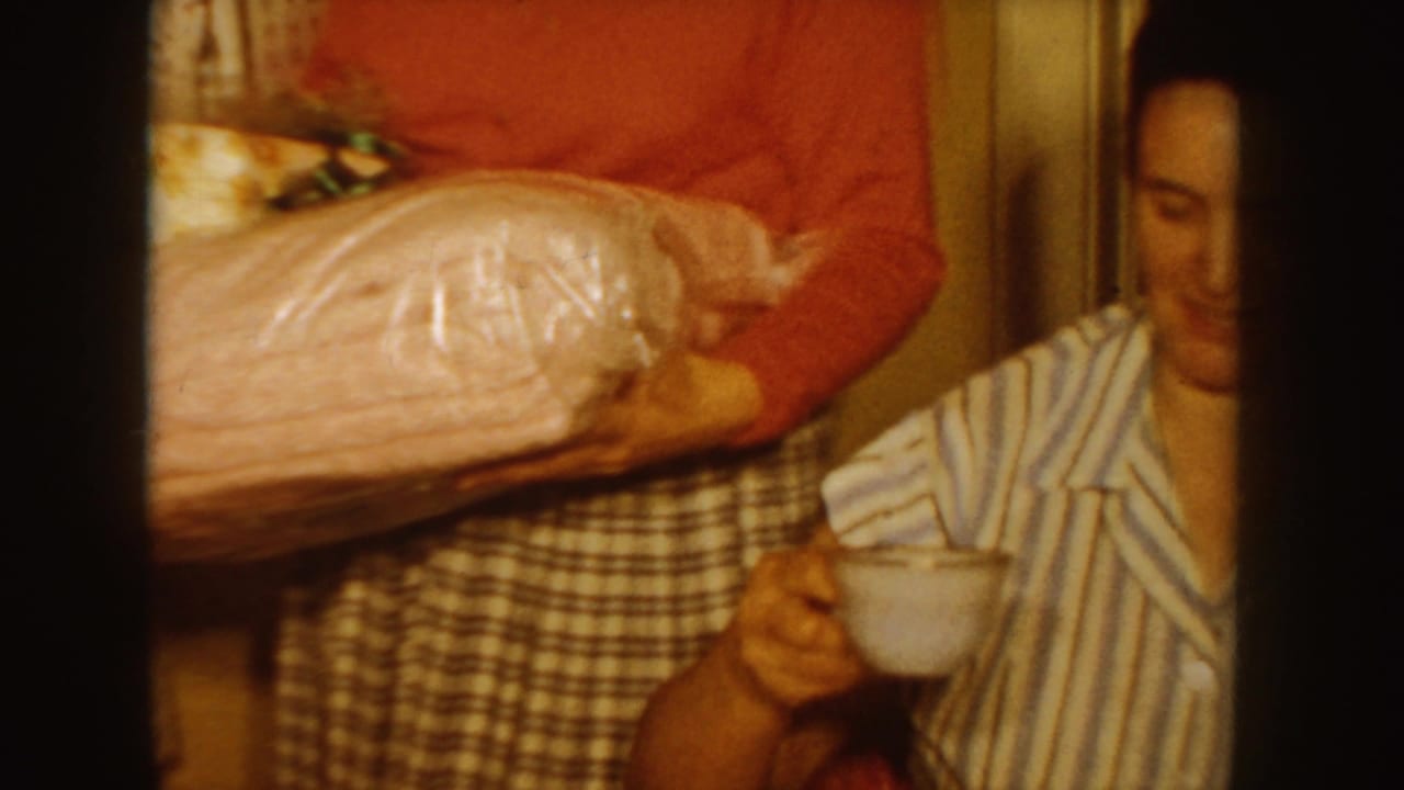 Woman carrying wrapped presents toward a seated girl in striped pajamas.