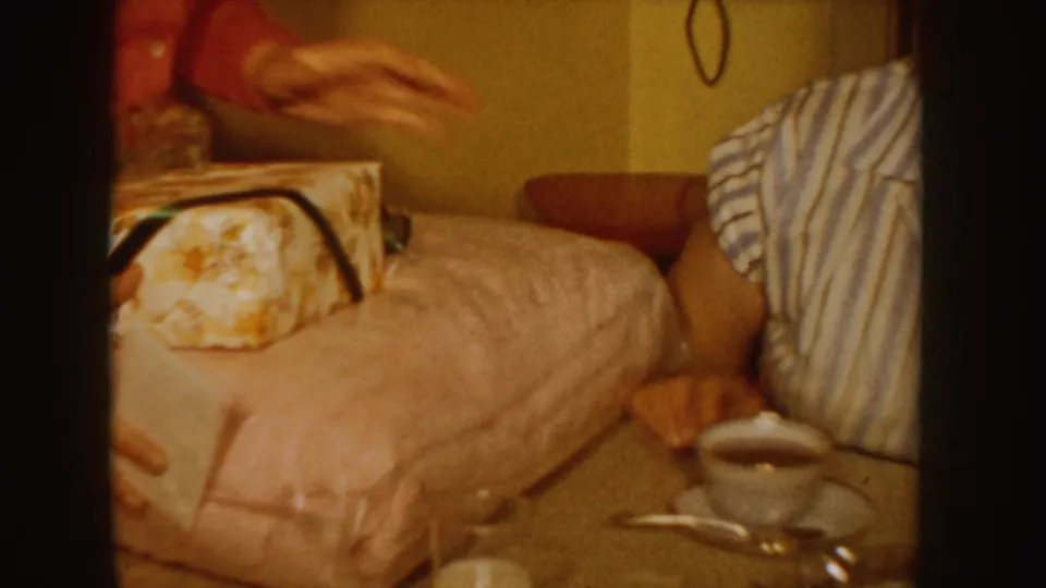 Close 1955 Idaho home-movie view of a wrapped present set near bedding, with a cup and saucer on the table below.