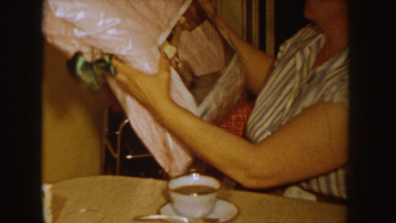 Woman in a striped shirt holds a plastic-wrapped item at a kitchen table.