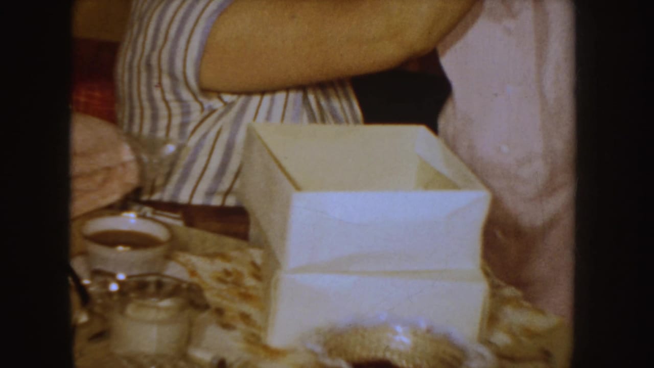 Woman in striped blouse sits by a white box on a patterned table with a pink garment nearby.