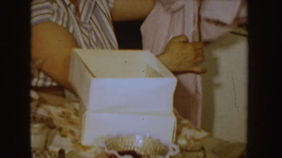 1955 Idaho home interior with a woman holding a pink garment beside an open white gift box on the table.