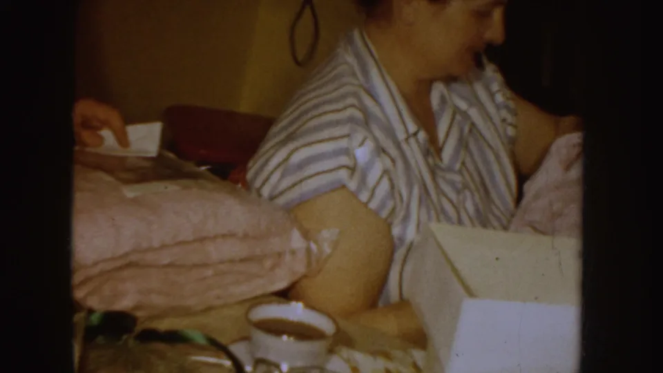1955 Idaho frame showing the woman turned in profile with the pink garment and white box in a close home setting.