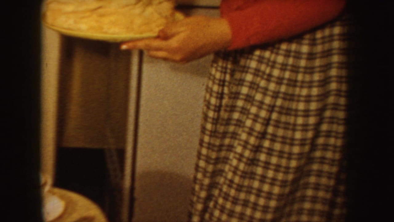 Woman in a red shirt and plaid skirt holds a white cake near a table.