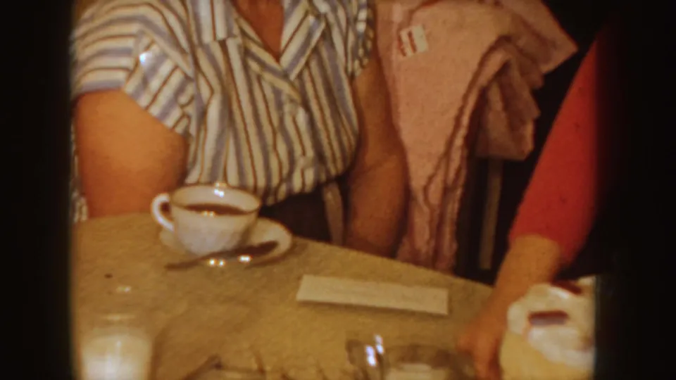 A seated person in a striped blouse appears beside cups and a glass on the tan table during the home celebration.