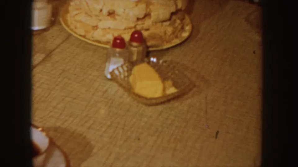 The frosted cake rests on the tan table near red-topped shakers, a glass of milk and a small plate in the Idaho home interior.