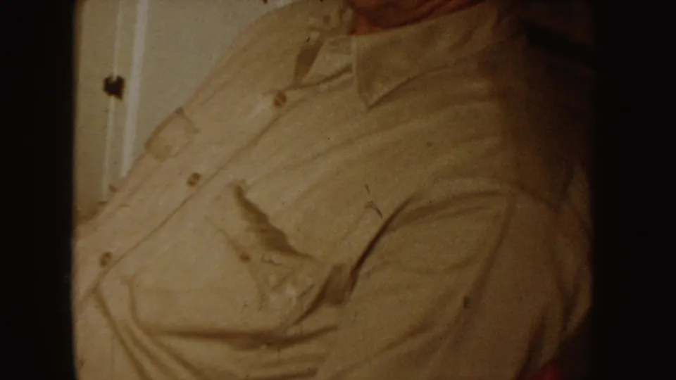 1955 Idaho 8mm frame showing a close, cropped view of a person in a light collared shirt inside a private domestic interior.