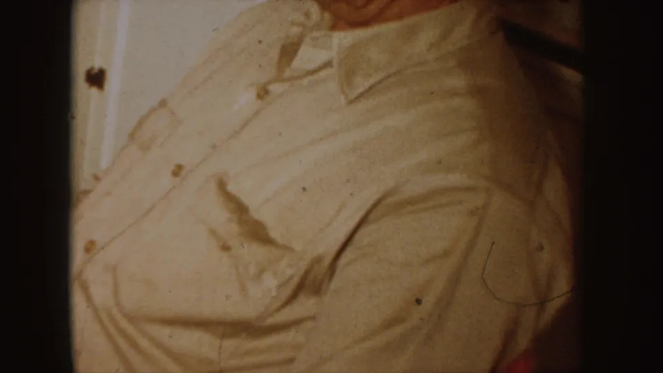 1955 Idaho home-movie frame with a cropped adult figure in a light collared shirt near interior trim, filmed in warm 8mm color.