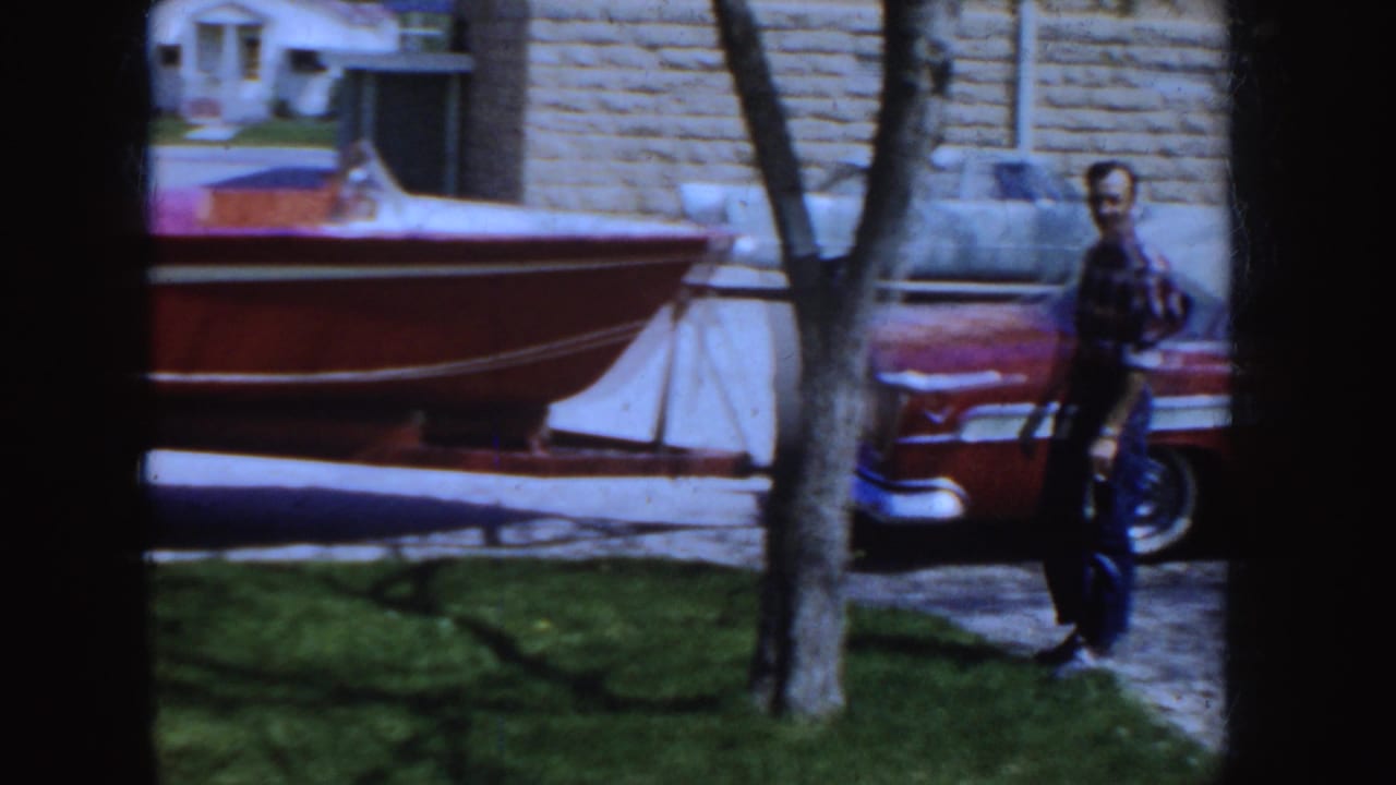 Man standing near a red-and-white car and a trailered boat outside.