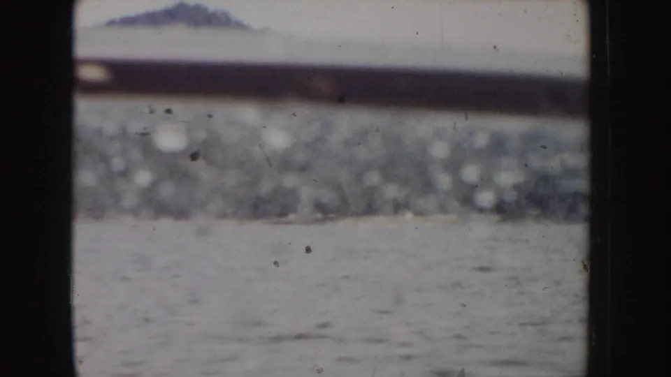 1955 Idaho 8mm frame showing a muted lake surface and far mountain ridge viewed through dark horizontal and vertical rails.