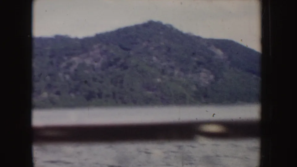 1955 Idaho 8mm frame showing a closer view of a forested mountain slope above the lake, partially obscured by dark rails.