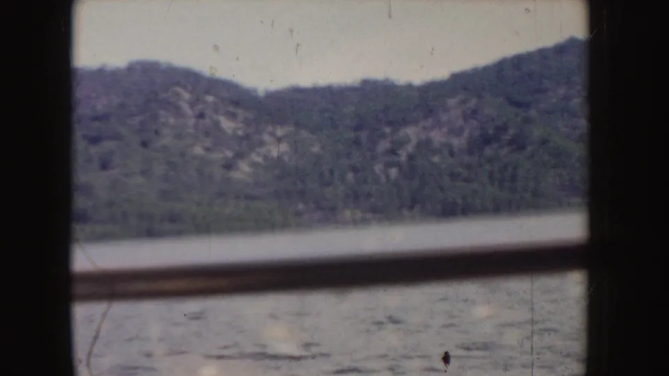 1955 Idaho 8mm frame of a distant mountain ridge and lake surface, divided by dark rails with visible film wear.