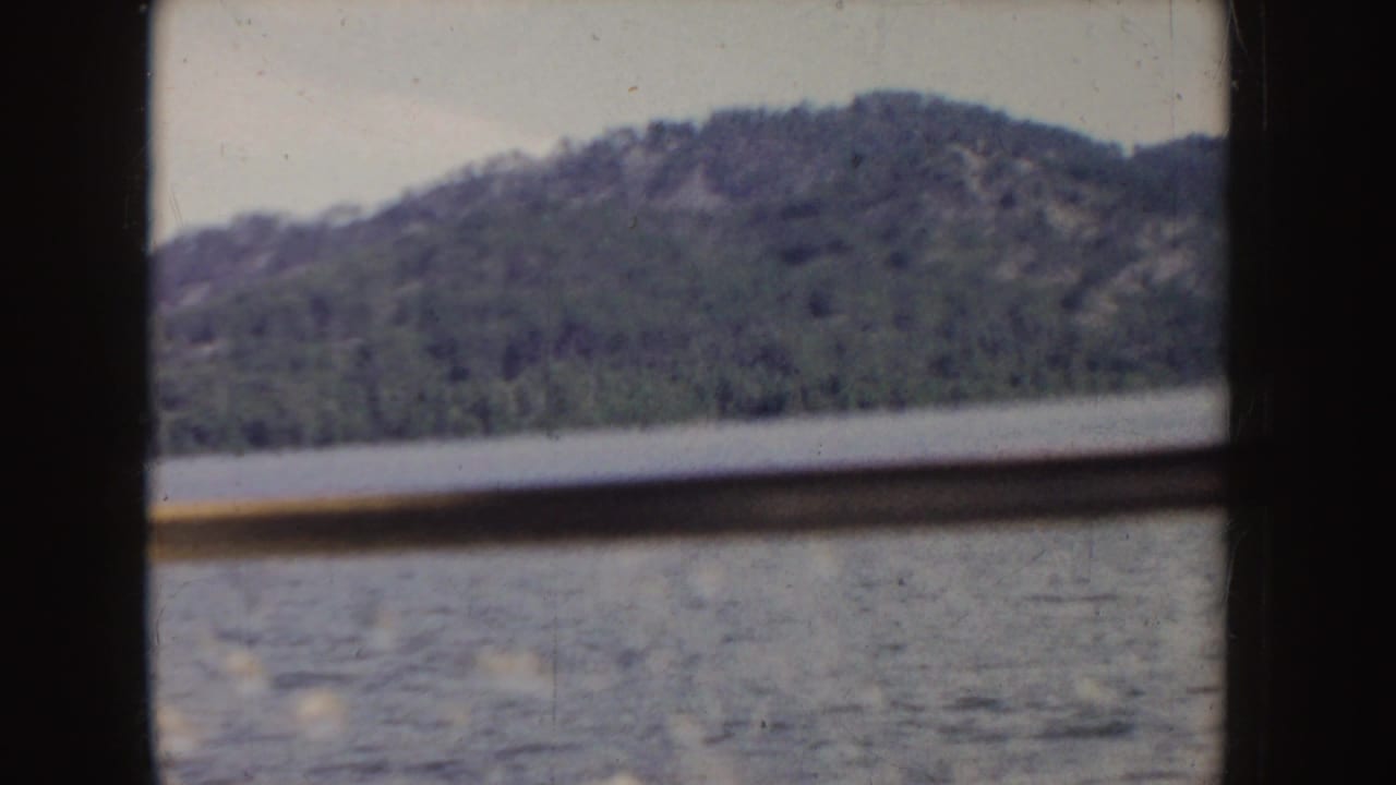 Forested hillside and lake water seen through dark boat or window framing.