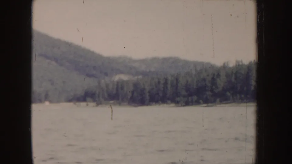 1955 Idaho lake scene showing open water, a forested shoreline, and soft green hills in faded 8mm color.