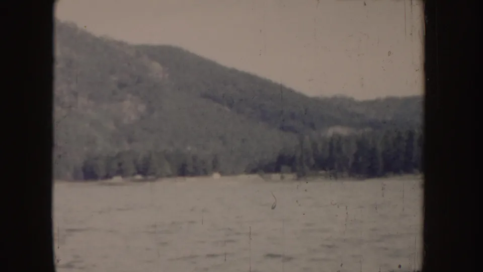 1955 Idaho 8mm frame with distant forested hills, calm water, and a lightly faded home-movie palette.