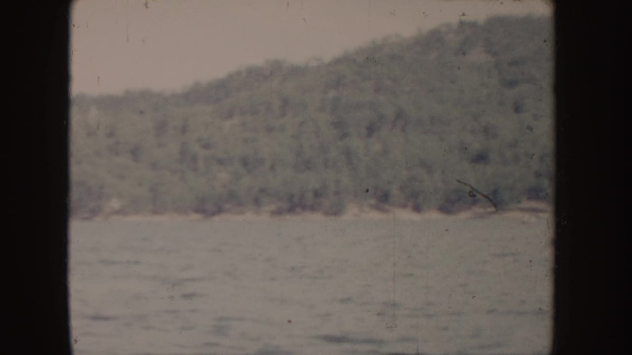 1955 Idaho 8mm frame looking across lake water toward a wooded hillside and distant shore.