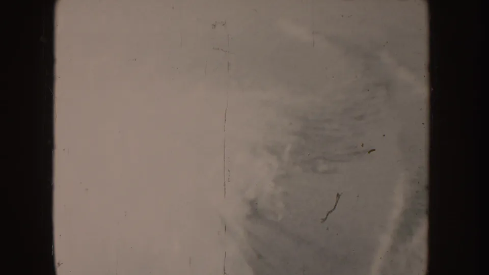 Faded 8mm frame from the Idaho boating clip, showing boat surfaces, dark framing, and a partial blurred view toward flag and water.