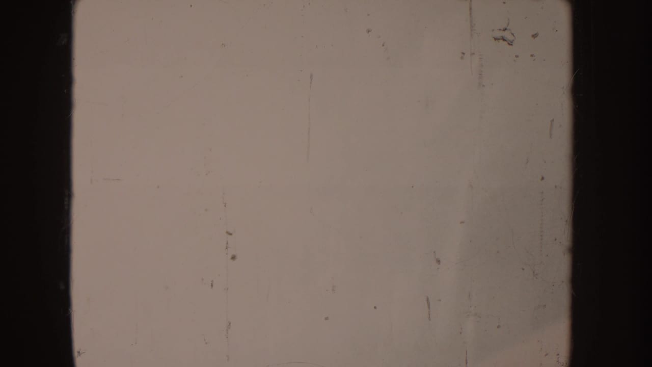 Damaged 1955 Idaho 8mm home-movie frame with off-white exposure, dark gate edges, dust, scratches, and a central black divider.