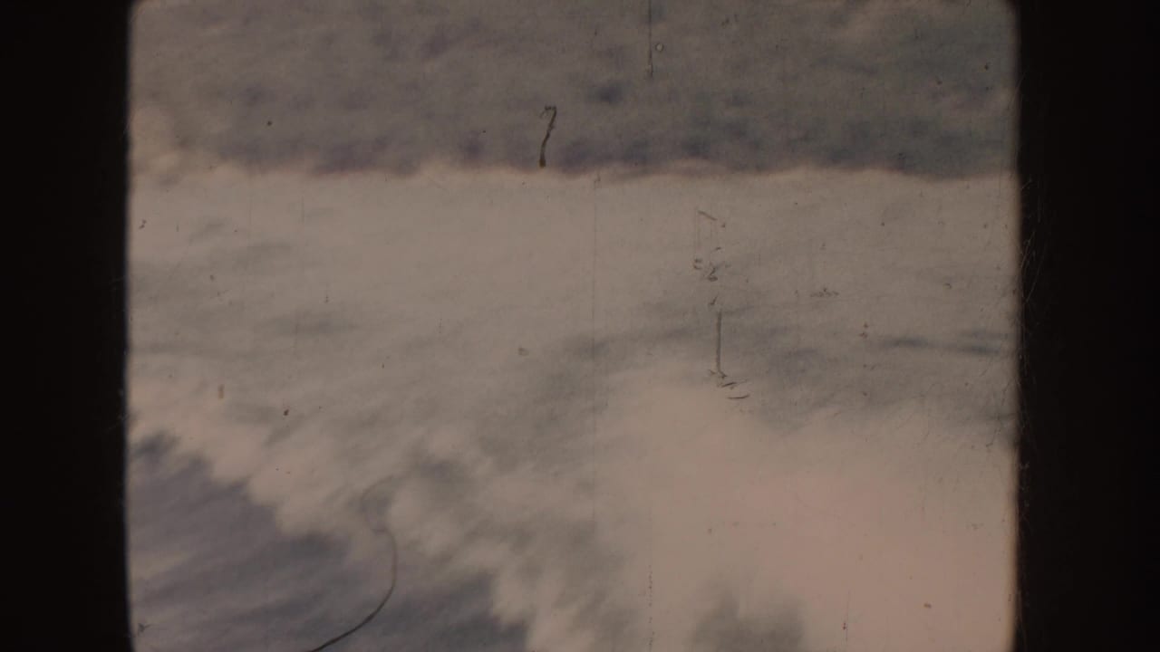 1955-attributed 8mm home-movie frame showing rough foamy water with dark wave bands and visible film scratches.