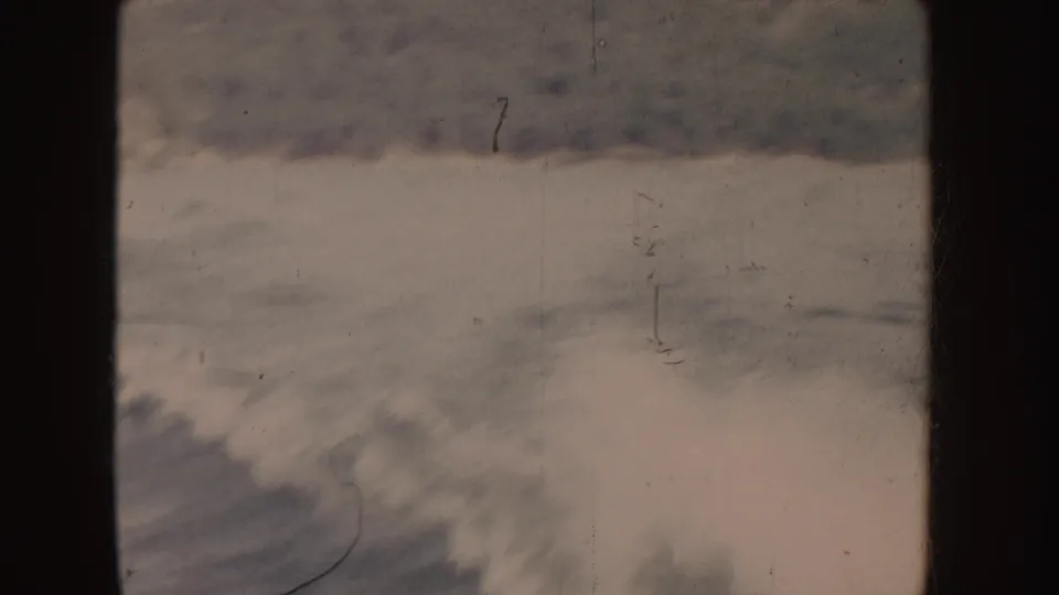 1955-attributed 8mm home-movie frame showing rough foamy water with dark wave bands and visible film scratches.
