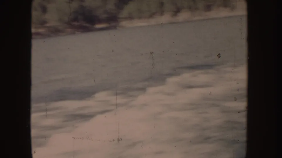 1955-attributed 8mm frame showing foamy water in the foreground and indistinct darker shoreline shapes in the distance.