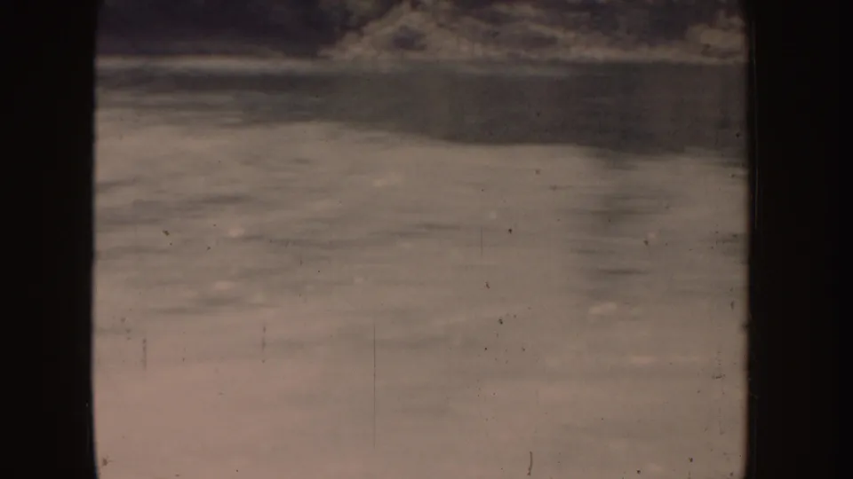 1955 Idaho 8mm frame of rippled lake water and a dark distant shoreline, seen from a moving boat.