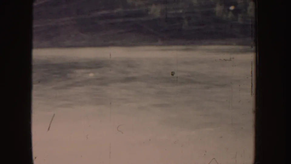 1955 Idaho 8mm frame showing wake lines and spray on lake water with a shadowed shoreline in the distance.