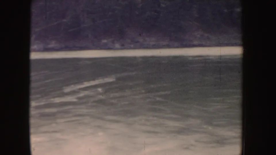 1955 Idaho 8mm frame of churning lake water, wake streaks, and a dark shoreline from a moving boat viewpoint.