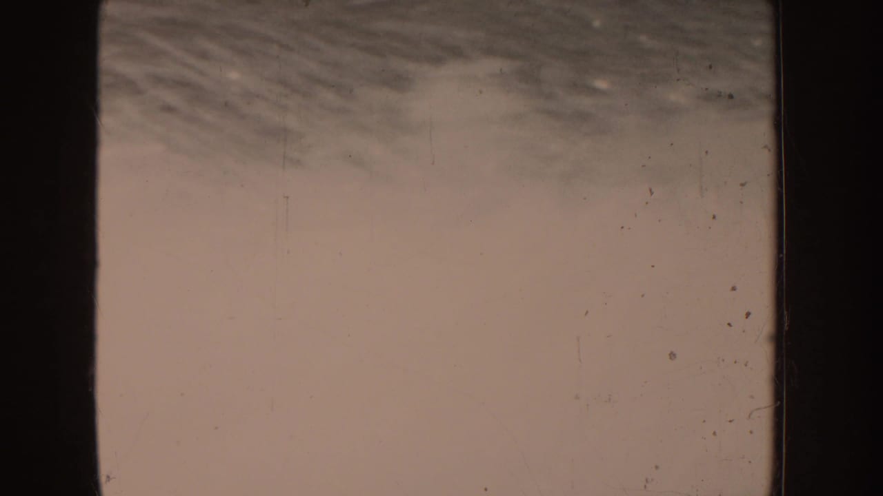 Mostly blank pale film frame with faint sky or water texture and specks.