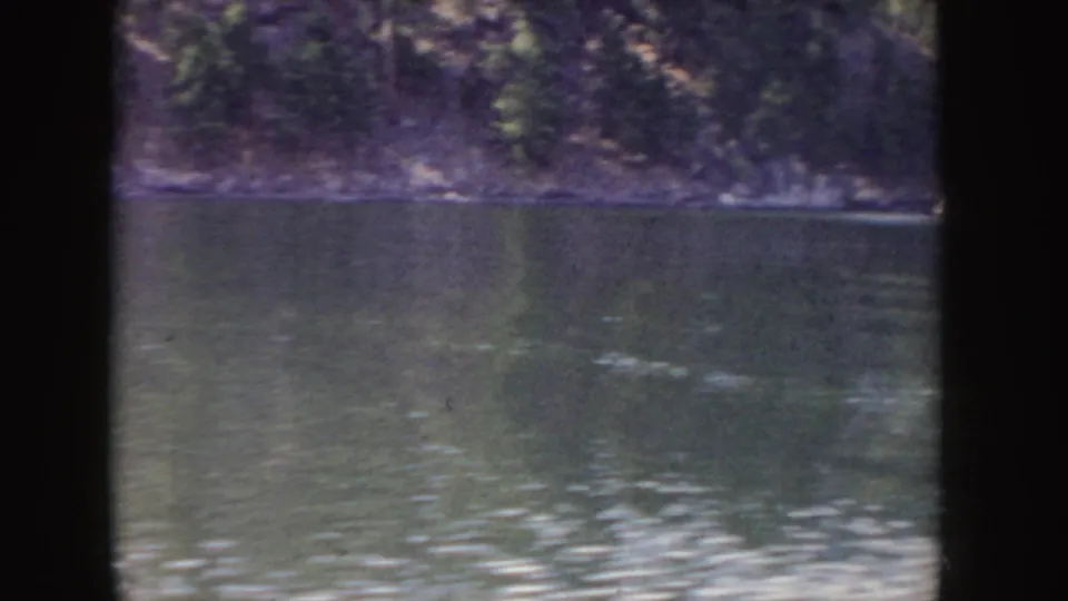1955 Idaho 8mm frame showing calm river water and a wooded far bank, with soft color and home-movie grain.