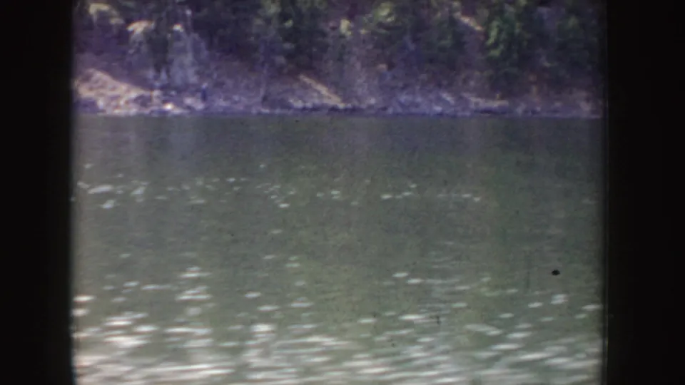Wide 8mm view of a river and forested Idaho shoreline, with visible fading, dust, and soft focus from the film scan.