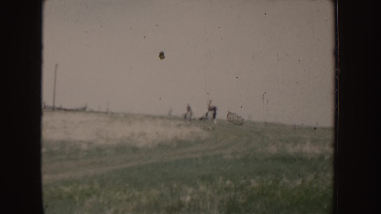 Two people ride horses across an open Idaho field in 1955 home-movie footage, seen at a distance through soft 8mm focus.