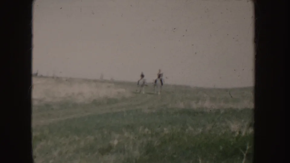 The two riders continue across the Idaho field, their horses and figures softened by motion and 8mm film grain.
