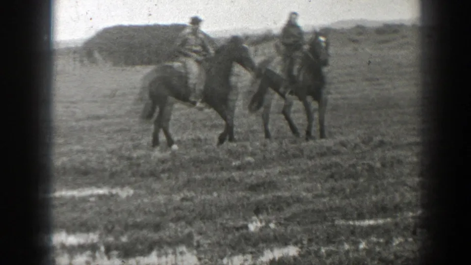 Two adults ride horses side by side in a grassy Montana field in 1939 home-movie footage.