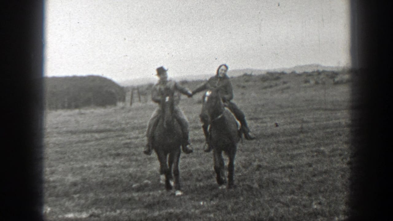 Two adults ride horses side by side across open grassland, with heavy film gate edges visible.