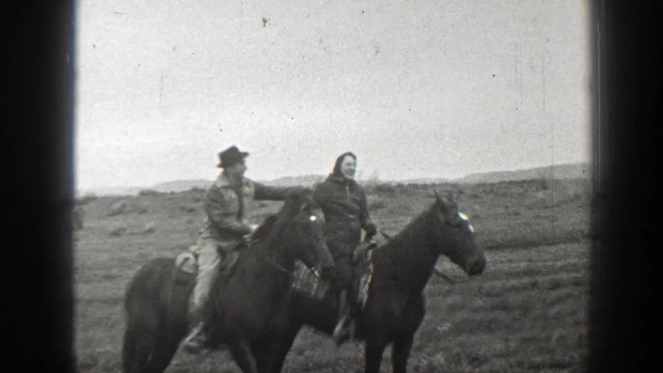 The couple rides close together on dark horses in the Montana landscape, with their upper bodies framed near the center of the 8mm image.