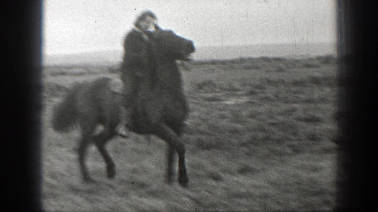 Person riding a horse across open grassland with dark film edges.