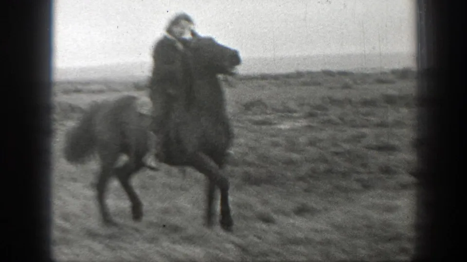 In 1939 Montana home-movie footage, a person rides a horse across open ranch land under a pale sky.